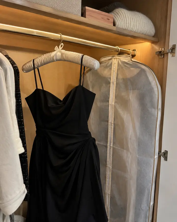 Black dress on a padded hanger in an open wardrobe next to a breathable garment bag