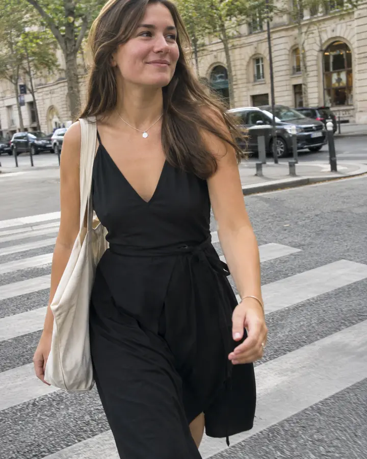 Woman in a black midi dress and white sneakers crossing a city street